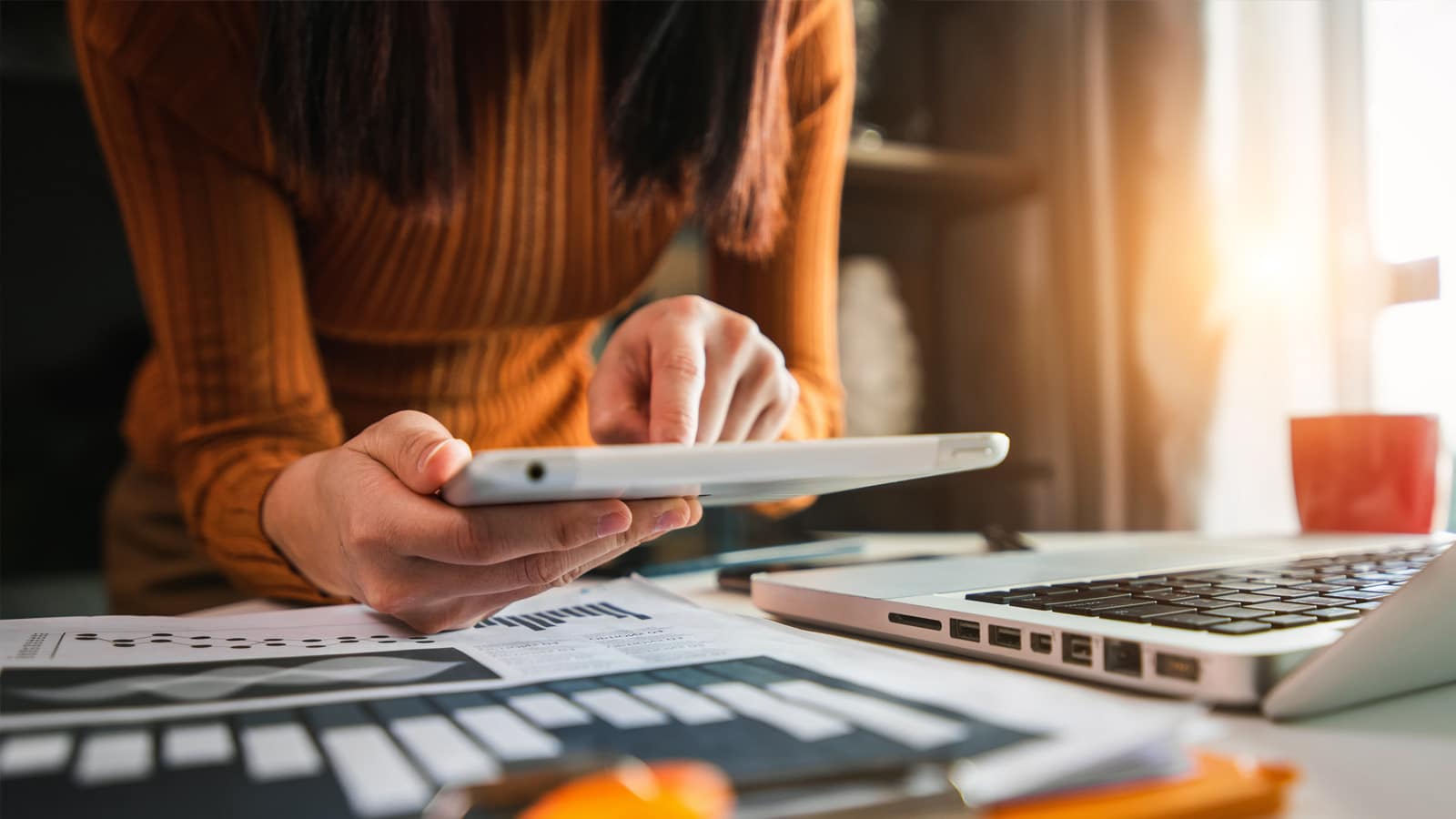 Bildet viser en person som jobber på en Ipad eller kalkulator med papirer rundt.